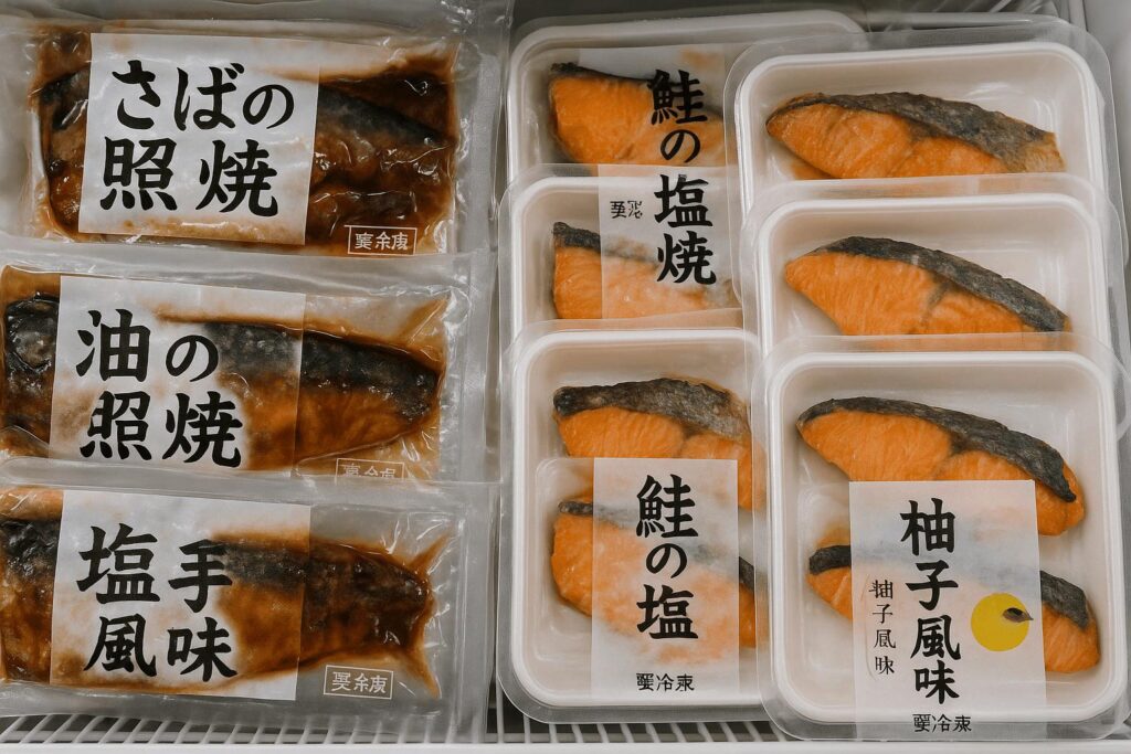 Frozen packs of grilled mackerel and salmon with yuzu flavor, displayed in a Japanese convenience store freezer